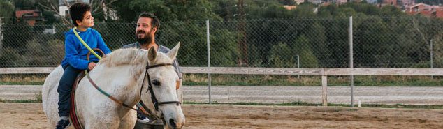 Child riding a white horse with adult walking at side