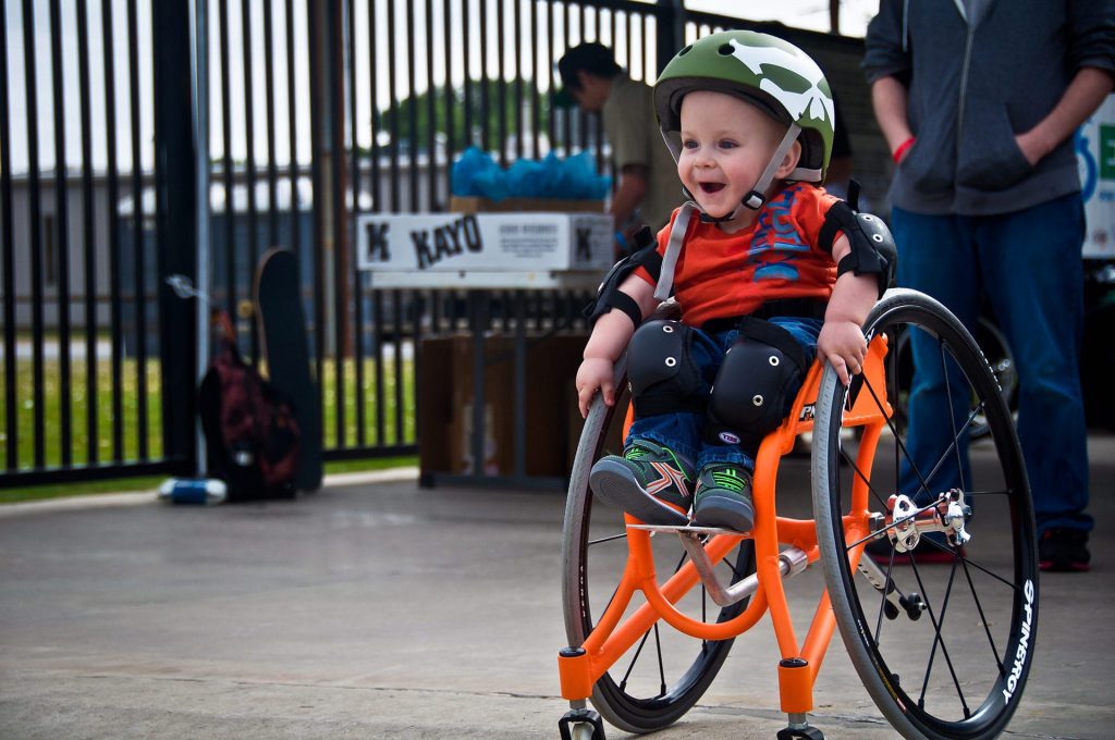 Young child in orange wheelchair smiling